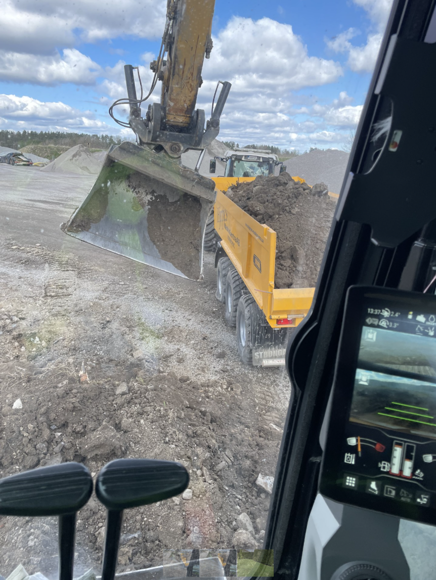 Grävmaskin som lastar jord i en gul dumper